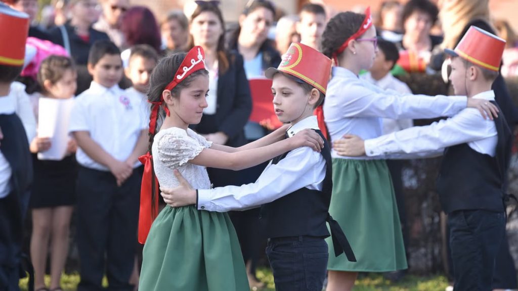 Children in costumes performing a traditional dance at an outdoor event, lively atmosphere.